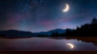 Crescent moon illuminates serene night sky above calm lake with mountain silhouettes and starry backdrop, creating tranquil nocturnal landscape for nature and astronomy themes.