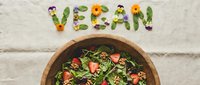 Fresh vegan salad with strawberries, walnuts, and greens in a wooden bowl, with the word vegan spelled out using edible flowers and leaves.