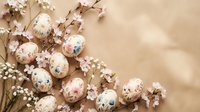 Delicate floral Easter eggs with vintage rose patterns nestled among white spring blossoms on warm beige background for holiday celebrations and decor.
