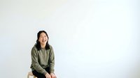 Young Asian woman wearing olive green jacket smiling at camera against white background, suitable for portrait, lifestyle, and business applications.