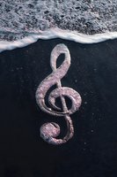 Treble clef symbol made of pink glitter on dark wet sand with ocean waves washing ashore creating artistic music concept for creative projects.