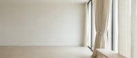Minimalist empty room with beige walls, wooden floor, and flowing cream curtains by large window, suitable for interior design and real estate projects.