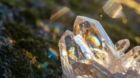 Clear quartz crystal cluster with rainbow light reflections on natural moss background creating magical healing energy and spiritual meditation atmosphere.