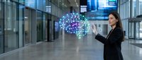 Young Asian businesswoman in black suit interacting with glowing digital brain hologram in modern office corridor, AI technology concept.