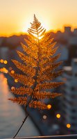 Golden fern leaf silhouetted against sunset sky with bokeh lights in background, creating magical autumn atmosphere for nature and seasonal designs.