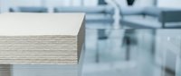 Stack of wooden boards or plywood sheets in modern workshop or factory setting with blurred industrial background for construction projects.