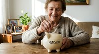 Happy elderly Caucasian woman saving money in piggy bank labeled pension at home. Senior female planning retirement finances and future security.