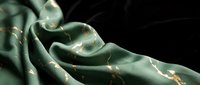 Luxurious sage green silk fabric with golden accents flowing elegantly against dark background for fashion and textile design projects.