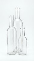 Three empty clear glass bottles of different sizes arranged together on white background for packaging design and beverage industry concepts.