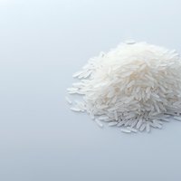 Raw white jasmine rice grains in pile on light gray background, minimalist food photography composition with copy space for text or design elements.