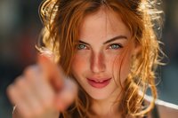 Young woman with vibrant red hair and striking blue eyes in warm sunlight, reaching toward camera with soft focus background.