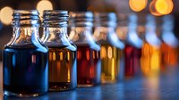 Glass bottles with colorful liquids in row, backlit with bokeh lights creating atmospheric bar or laboratory setting, selective focus on front bottles.