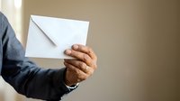Close-up of male hand holding sealed white envelope against neutral background, suitable for business correspondence, mail delivery, and communication concepts.