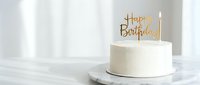 White birthday cake with golden Happy Birthday topper and lit candle on marble stand, minimalist elegant celebration dessert for party.