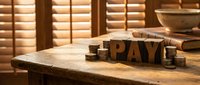 Wooden letter blocks spelling pay arranged on rustic table with coins and financial documents, symbolizing taxation, payroll, salary and accounting concepts for business and finance.