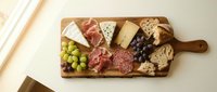 Gourmet charcuterie board with assorted cheeses, cured meats, grapes, nuts and crackers on wooden serving platter for entertaining and appetizers.