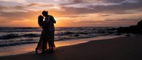 Romantic couple silhouette embracing on beach at sunset with golden sky and ocean waves creating intimate moment for love and relationship concepts.
