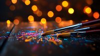 Paint brushes on glittering surface with golden bokeh lights in background creating magical artistic atmosphere. Shallow depth of field enhances dreamy effect.