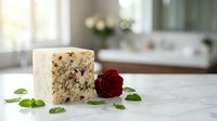 Young woman with fair complexion and long dark hair, wearing casual attire, holding a slice of fruit cake with nuts and dried fruits, decorated with a red rose and mint leaves on marble surface.