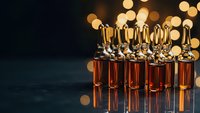 Medical glass vials with amber liquid and golden caps arranged in rows with warm bokeh lighting for pharmaceutical research and healthcare applications.