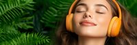 Young woman with orange wireless headphones relaxing with closed eyes among green fern leaves, enjoying peaceful meditation and music in nature.