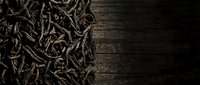 Dried tea leaves scattered on dark wooden surface with copy space for beverage packaging, culinary content, and tea product marketing.