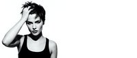 Young woman with short black spiky hair, fair complexion, wearing black sleeveless top, hand touching head in confident pose, monochrome studio portrait.