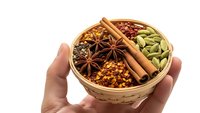 Hands holding wooden bowl with aromatic spices including cinnamon sticks, star anise, cardamom pods and chili flakes for cooking and seasoning.