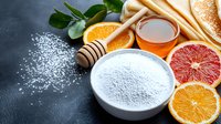 Fresh citrus fruits with honey, flour in white bowl and wooden dipper on dark background, top view. Natural baking ingredients for homemade pastry.