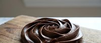 Rich chocolate frosting swirl on wooden surface for baking and dessert projects. Smooth ganache texture for culinary designs and food photography.
