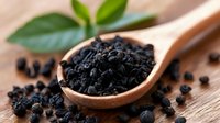 Black nigella sativa seeds in wooden spoon on rustic wooden background with fresh green leaves. Natural organic spice and herbal medicine ingredient.