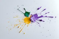 Vibrant paint splatter in green, yellow and purple colors creating dynamic abstract composition on white background, artistic expression through liquid medium.