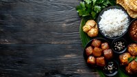 Asian meatballs with rice and various sauces served on black plate with banana leaf. Traditional oriental cuisine on dark wooden background with copy space.