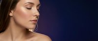 Young Caucasian woman with natural makeup and glowing skin against dark blue gradient background for beauty and skincare advertising campaigns.