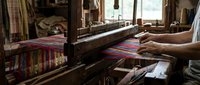 Traditional handloom weaving with colorful textile threads on wooden loom, artisan hands creating ethnic fabric patterns in rustic workshop setting.