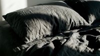 Unmade bed with crumpled gray and black pillows and wrinkled bedding in natural light, suitable for lifestyle, home decor, and bedroom design projects.