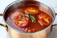 Fresh tomato soup with whole cherry tomatoes and basil leaves in copper cooking pot, close up view showing rich red broth and aromatic ingredients.