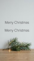 Minimalist Merry Christmas greeting card with pine branch and fairy lights on wooden surface, soft neutral background for holiday design use.
