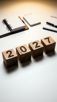 Wooden blocks displaying 2027 numbers arranged on white desk with notebooks and pens for new year planning and goal setting workspace.
