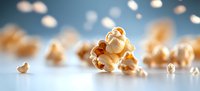 Popped corn kernels scattered on blue surface with soft bokeh lighting effect, macro food photography showing texture and detail of fresh popcorn snack.
