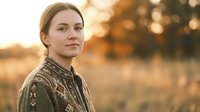 Young Caucasian woman in patterned sweater smiling outdoors during golden hour sunset with warm bokeh background for lifestyle and portrait concepts.