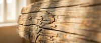 Weathered wooden beam with natural cracks and grain texture in warm lighting. Rustic construction material for interior design and architectural projects.