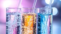 Colorful carbonated drinks in tall glasses with straws against blurred purple background, refreshing summer beverages with fizzy bubbles rising in clear liquid.