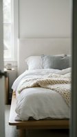 Cozy minimalist bedroom with unmade bed, chunky knit blanket, linen bedding and morning coffee cup on wooden nightstand creating hygge atmosphere.