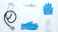 Medical equipment flat lay with stethoscope, disposable blue nitrile gloves, digital thermometer and hand sanitizer bottle on white background for healthcare.