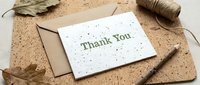 Eco-friendly thank you card with kraft envelope on cork board, surrounded by autumn leaves, twine, and pencil. Natural, sustainable stationery concept.