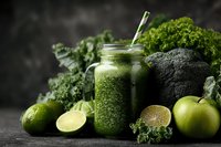 Green detox smoothie in glass jar with kale, broccoli, apple and lime against dark background, healthy nutrition concept.