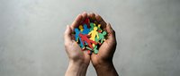 Hands holding colorful puzzle pieces forming heart shape symbolizing unity, teamwork, collaboration and problem solving in business and relationships.