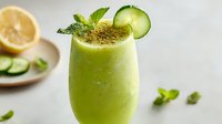 Fresh green cucumber smoothie with mint garnish and lemon slice, served in elegant glass on light background for healthy lifestyle promotion.