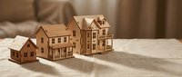Wooden miniature house models arranged on a linen surface in warm light, symbolizing real estate growth and property investment concepts.